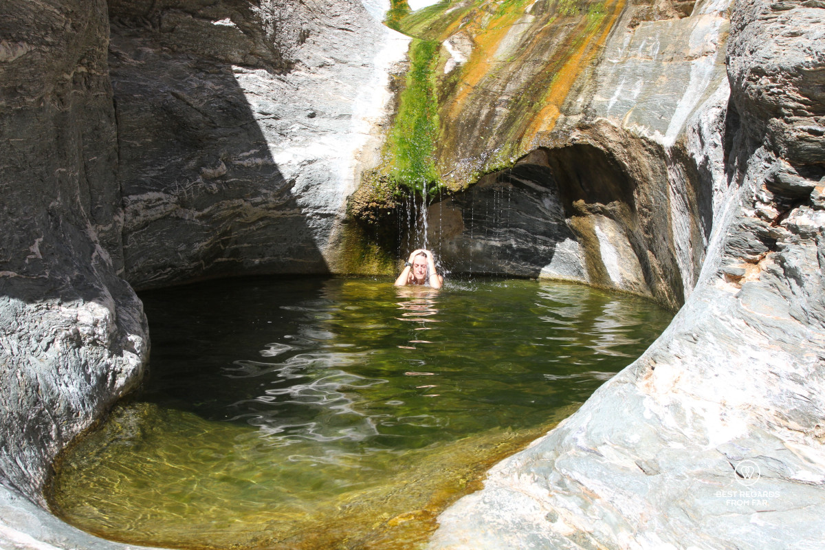 Woman cooling down in a rock pool, wetting her head underneath a small waterfall.