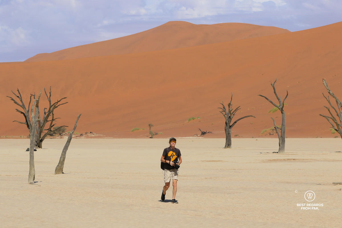 Photographer and author Claire Lessiau walking among dead trees with a red dune in the background.