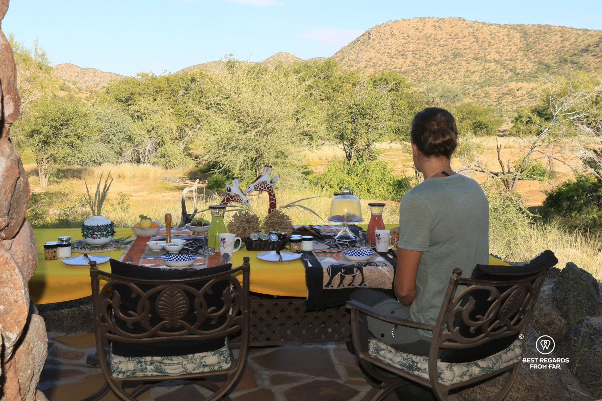Woman seated at a beautifully decorated breakfast table with a view on the dry riverbed, Namibia.