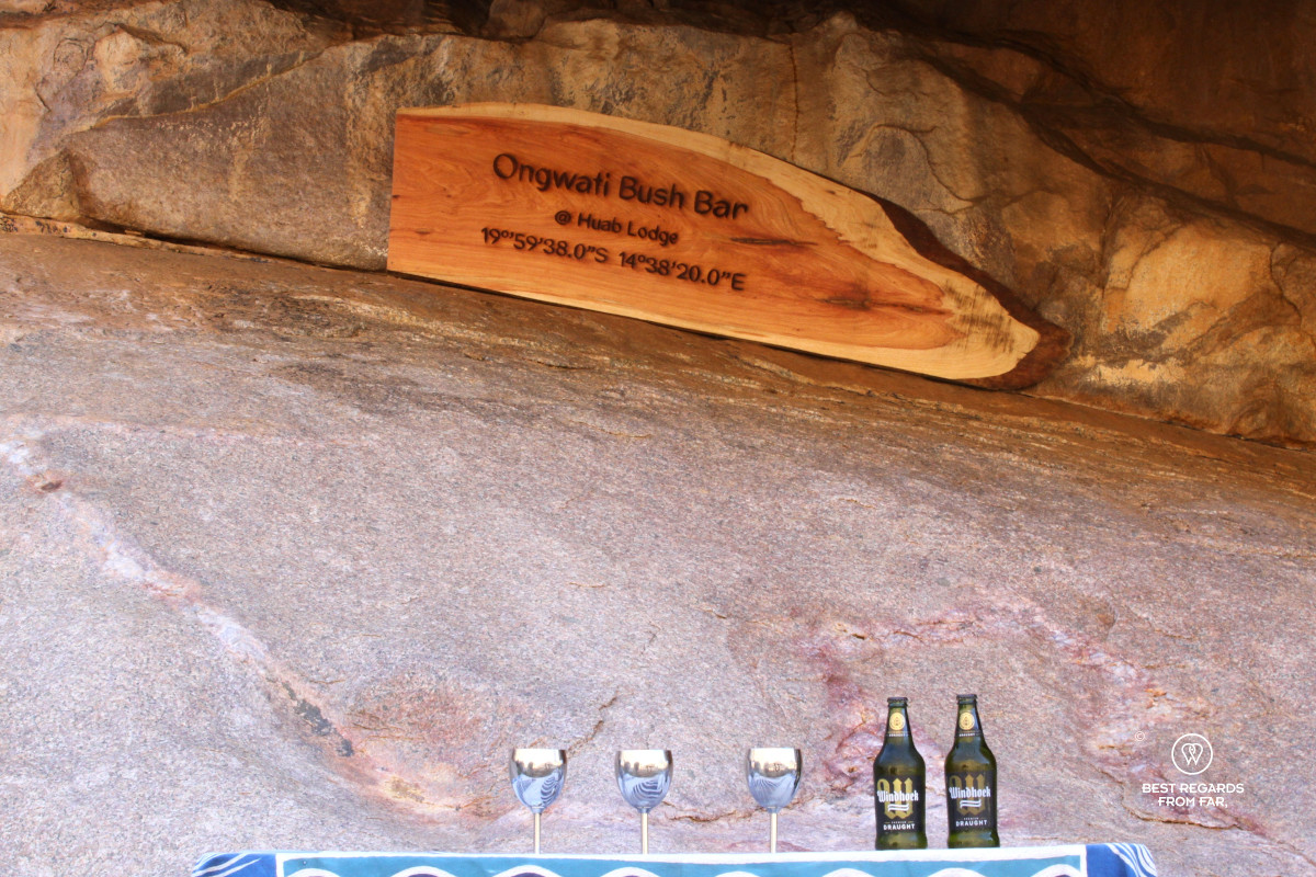 Two Winhoek Lagers and three glasses of win on a table under a rock overhand.