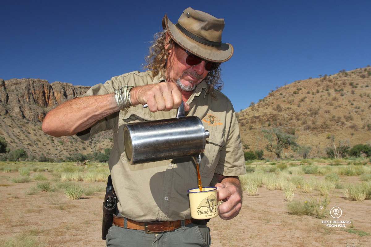 Huab Lodge owner Deon Brummer in khaki outfit pooring a coffee in a cup in the riverbed on a sunny day.