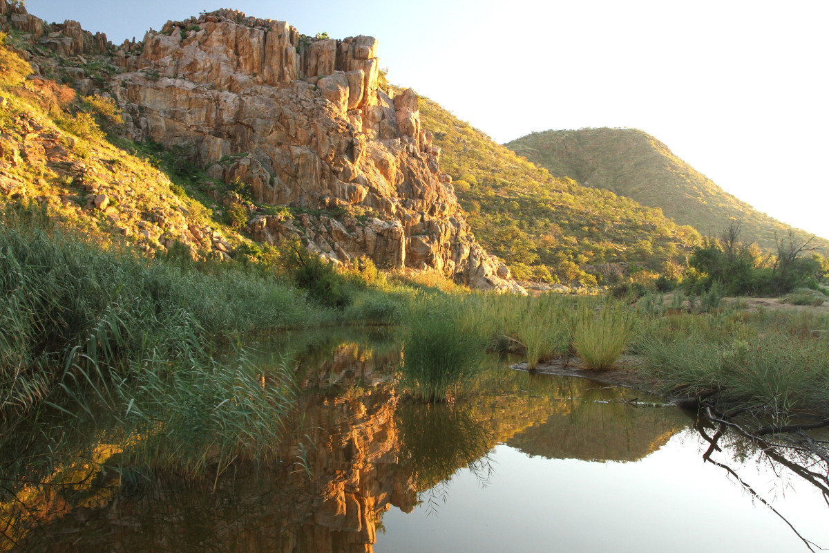 Rocky outcrop reflecting in the still waters of the Huab River, Namibia.