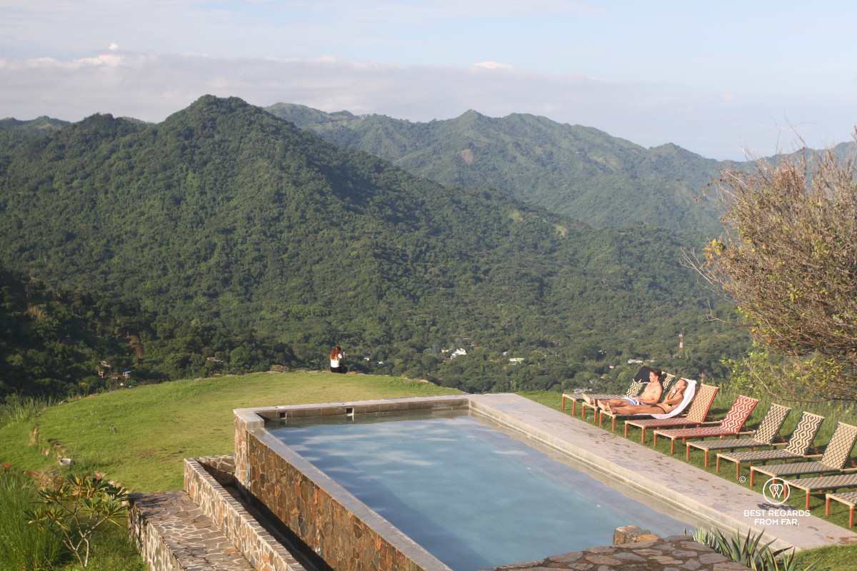 Swimming pool, sunbeds and people tanning with a view on green slopes of the Sierra Nevada de Santa Marta, Colombia.