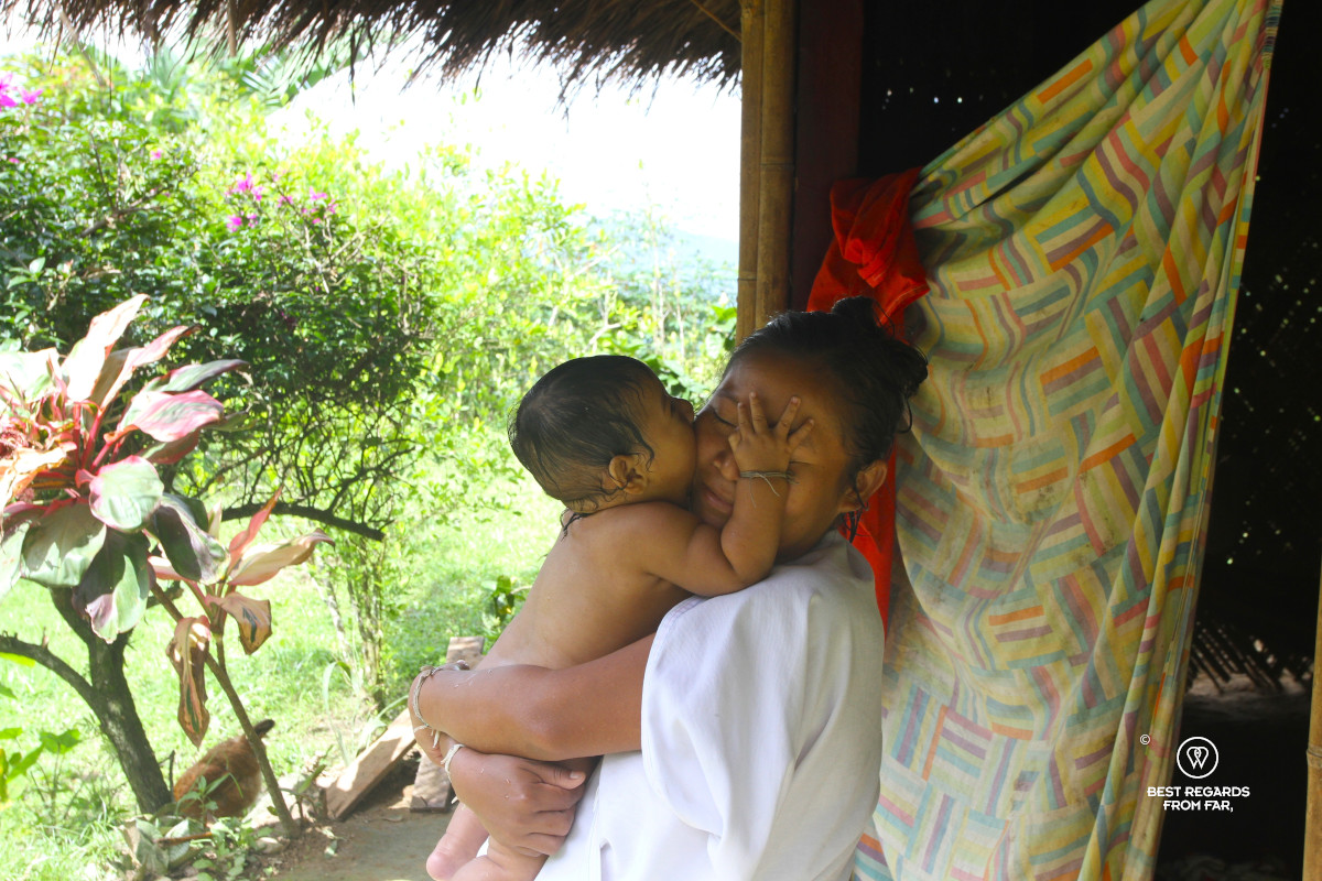 Wiwa woman dressed in white holding her baby in her arms in front of her home in Awindua, Colombia.