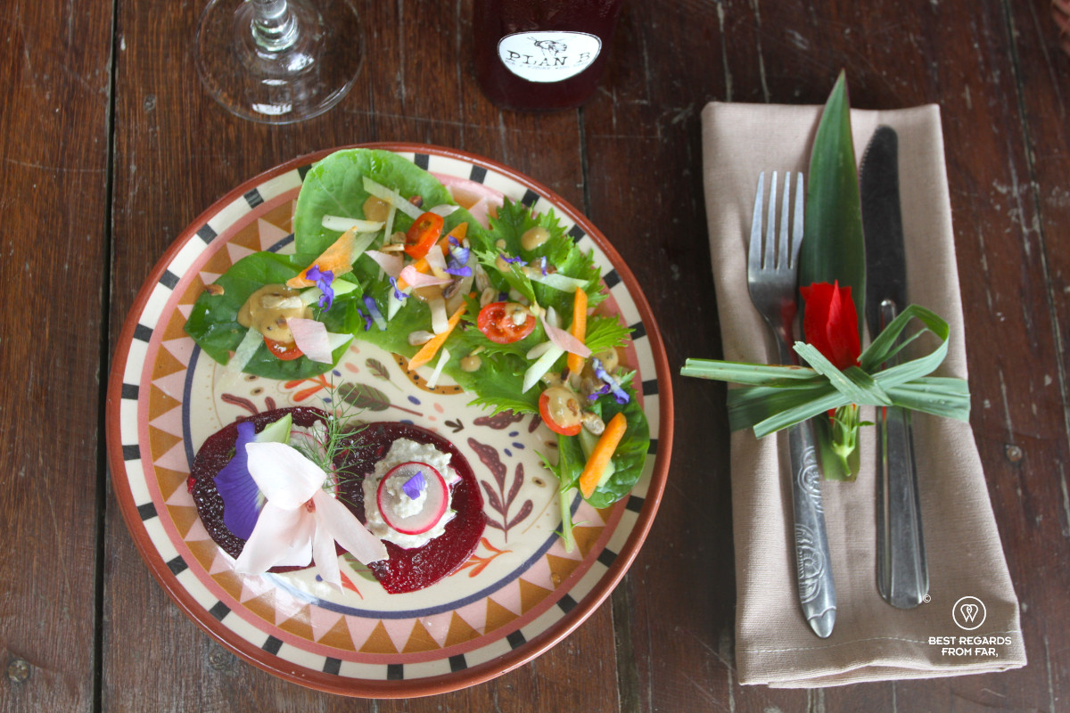 Colorful garden salad on a plate with cutlery dressed with a flower next to it.