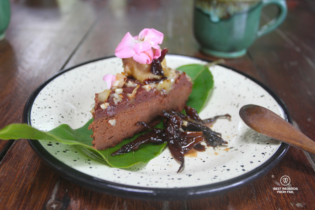 Raw chocolate cake decorated with flowers an served on a green leaf.