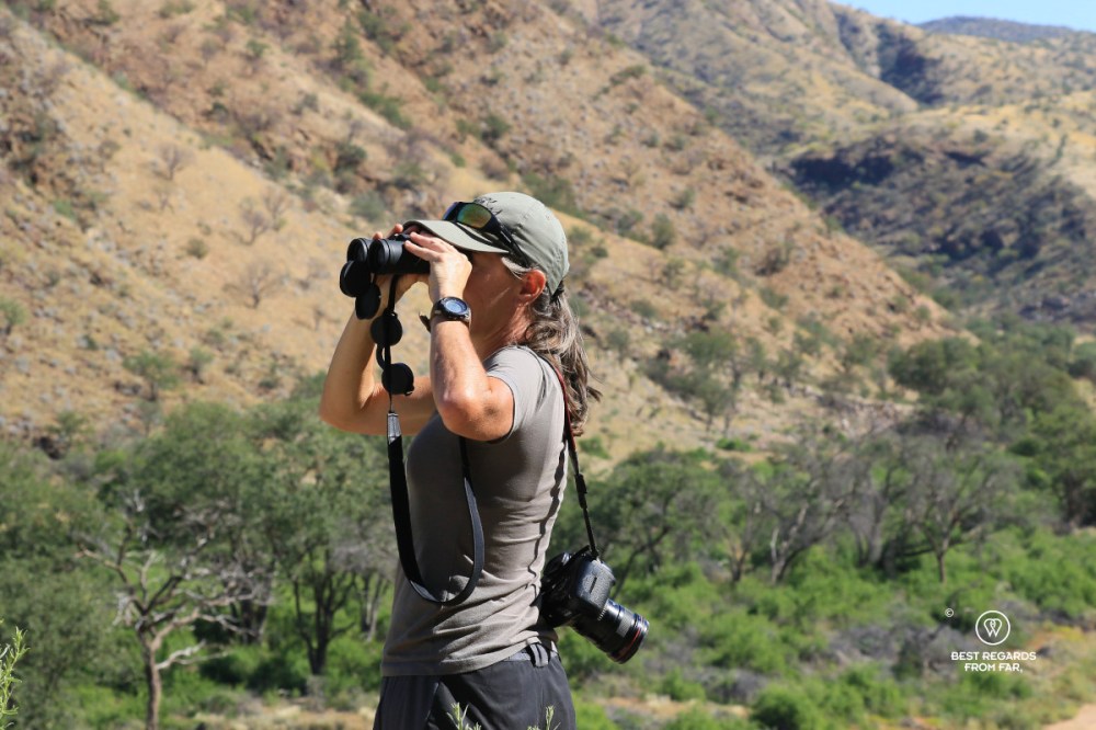 Author and photographer Claire Lessiau scanning for wildlife through a pair of binoculars in an arid landscape.