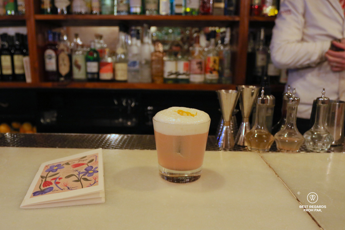 A pink cocktail with white foam on a bar.