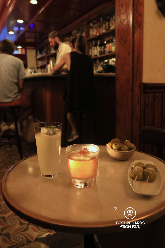Two cocktails, a plate of gildas and a bowl of olives in a bar.
