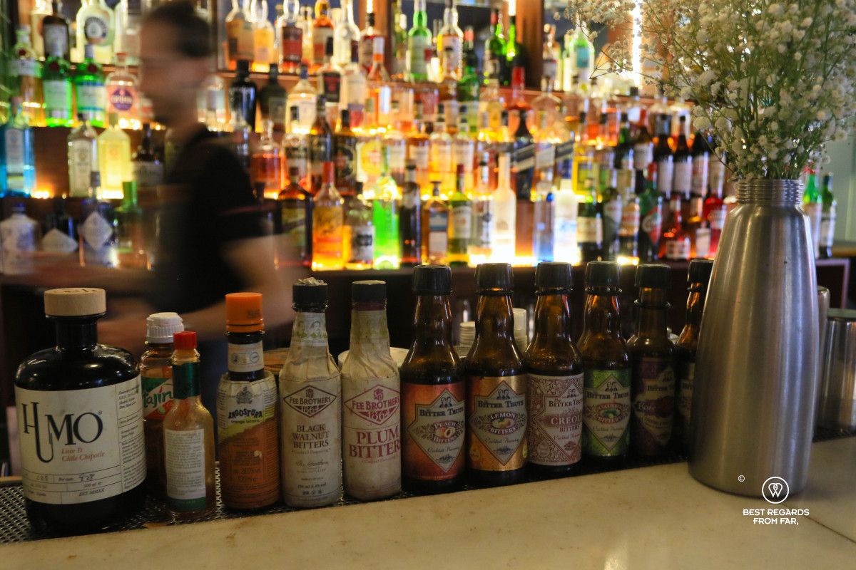 Bitters on a bar with bottles of alcohol in the background.