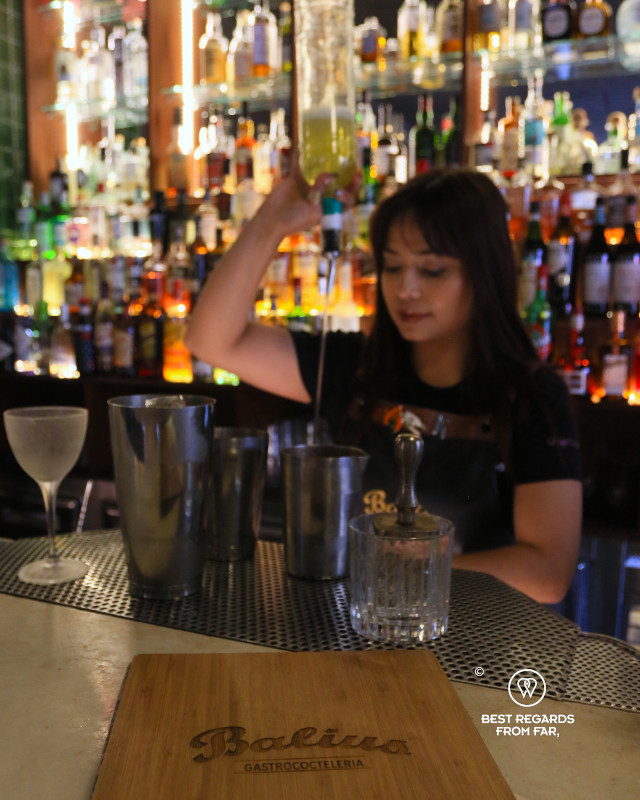 Female bartender preparing a cocktail with a smile.