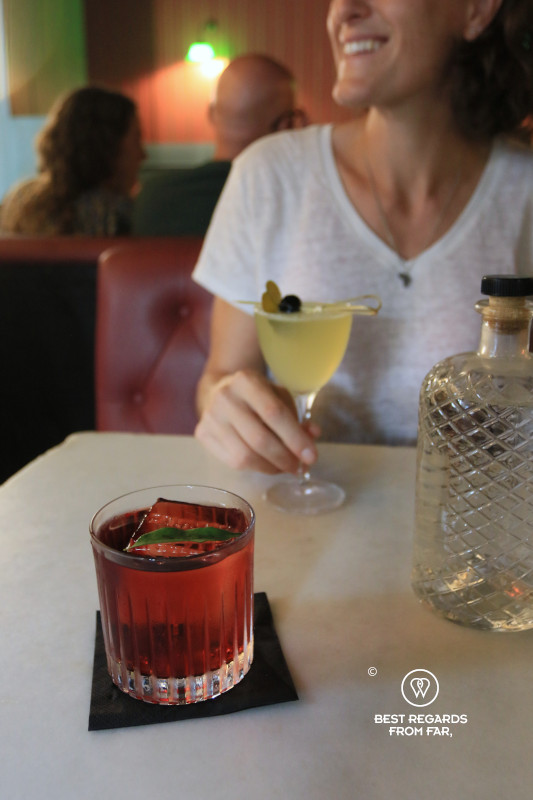 Two sleek and colorful cocktails and a bottle of water on a table.
