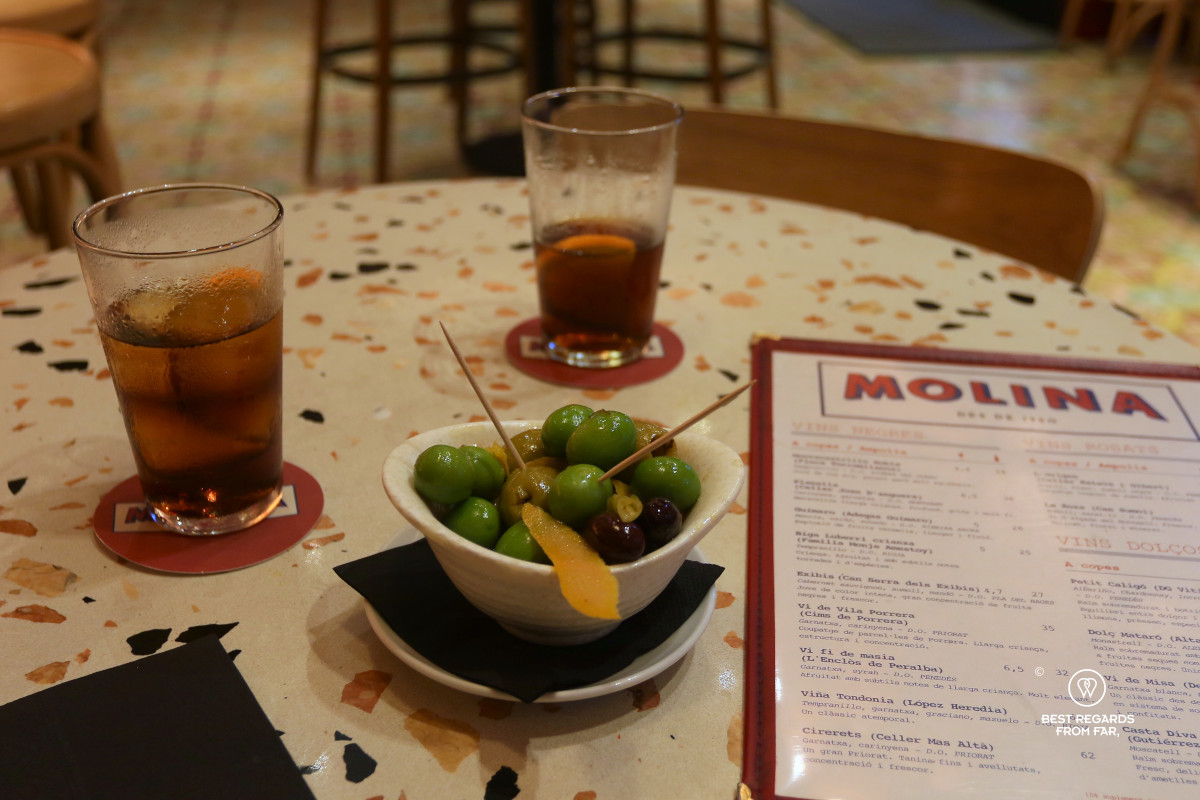 Two glasses of vermouth on a table with a menu and green olives.