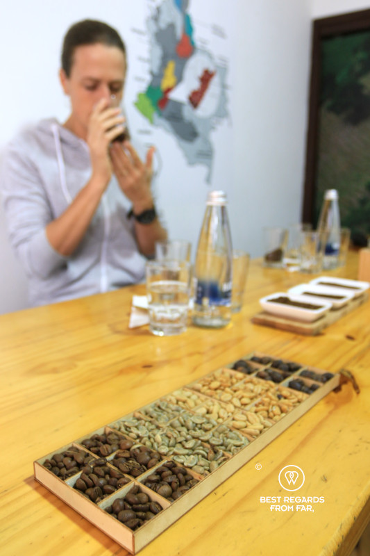 Different types of roasted coffee beans with someone in the background tasting coffee.